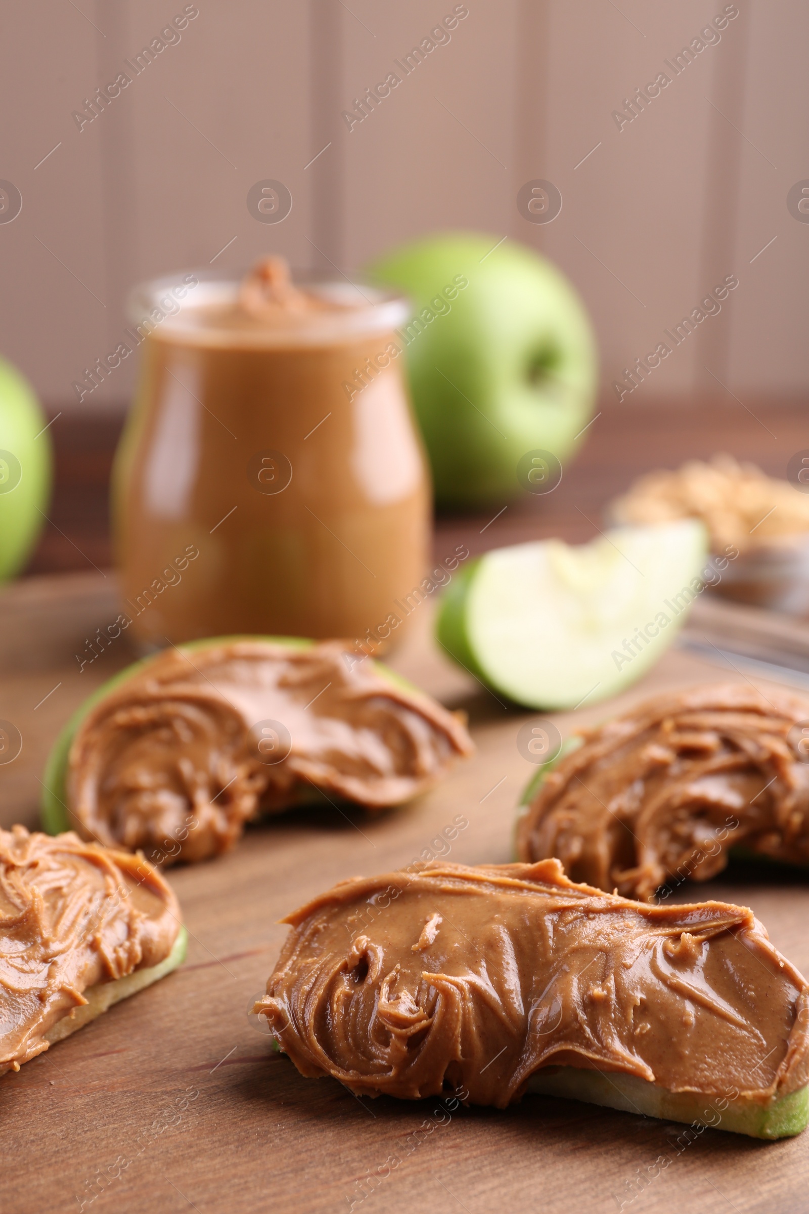 Photo of Slices of fresh green apple with peanut butter on wooden board, closeup