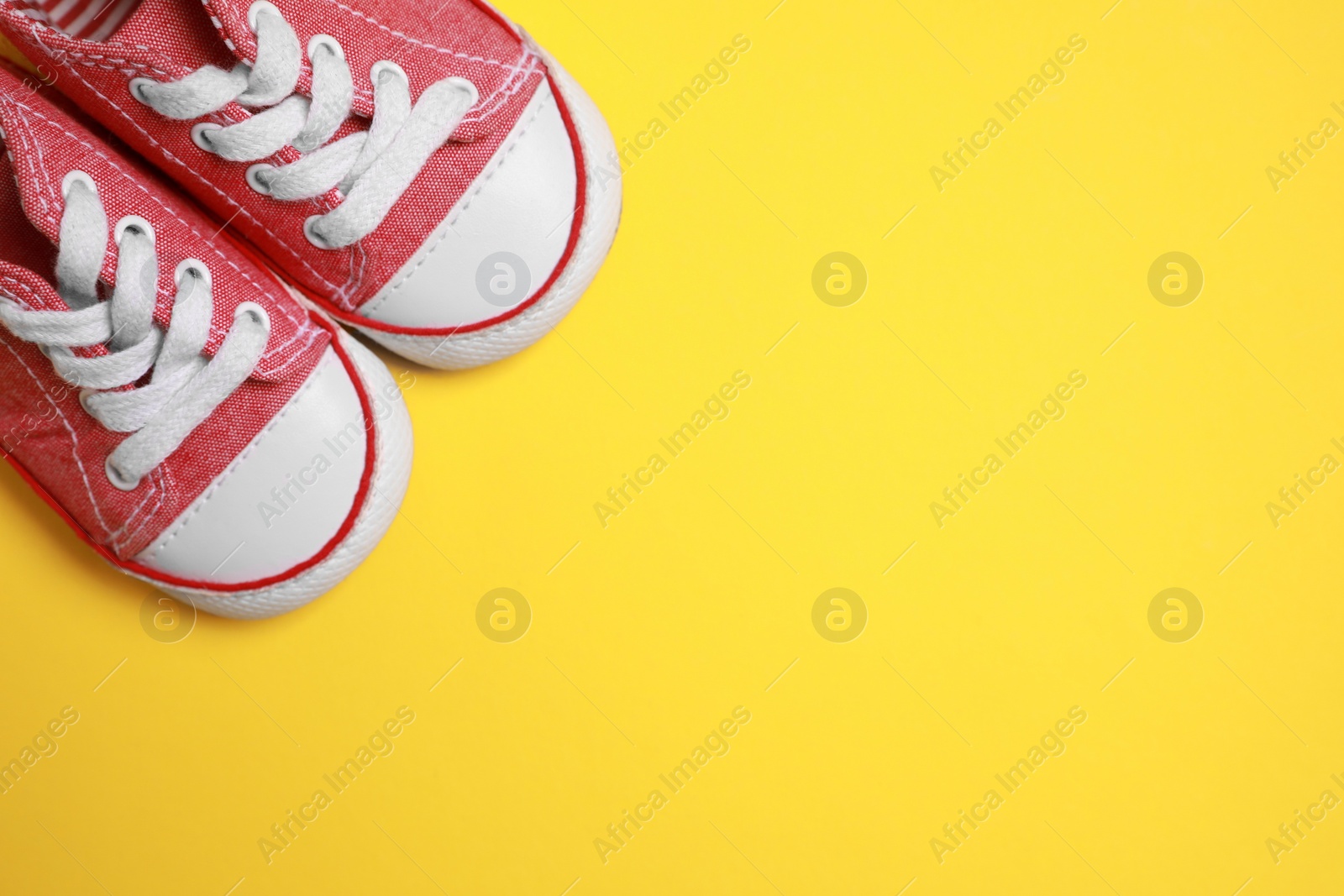 Photo of Cute baby shoes on yellow background, flat lay. Space for text