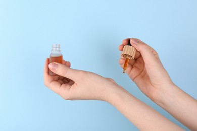 Photo of Woman applying essential oil onto wrist against light blue background, closeup