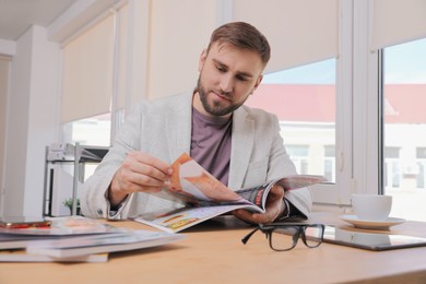 Photo of Young man reading modern magazine at table indoors