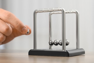 Photo of Man playing with Newton's cradle at table against light background, closeup. Physics law of energy conservation