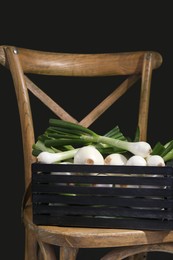 Photo of Crate with green spring onions on chair against black background