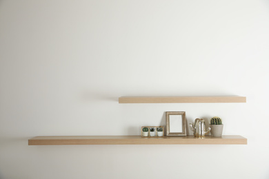 Photo of Wooden shelves with photo frame and decorative elements on light wall