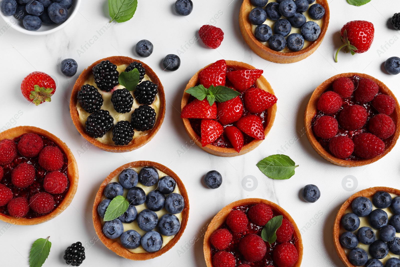 Photo of Tartlets with different fresh berries on white marble table, flat lay. Delicious dessert