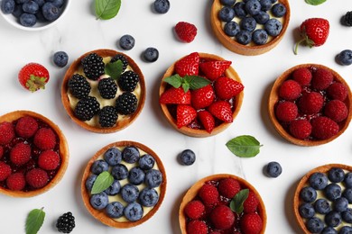 Photo of Tartlets with different fresh berries on white marble table, flat lay. Delicious dessert