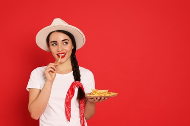 Beautiful young woman eating French fries on red background. Space for text