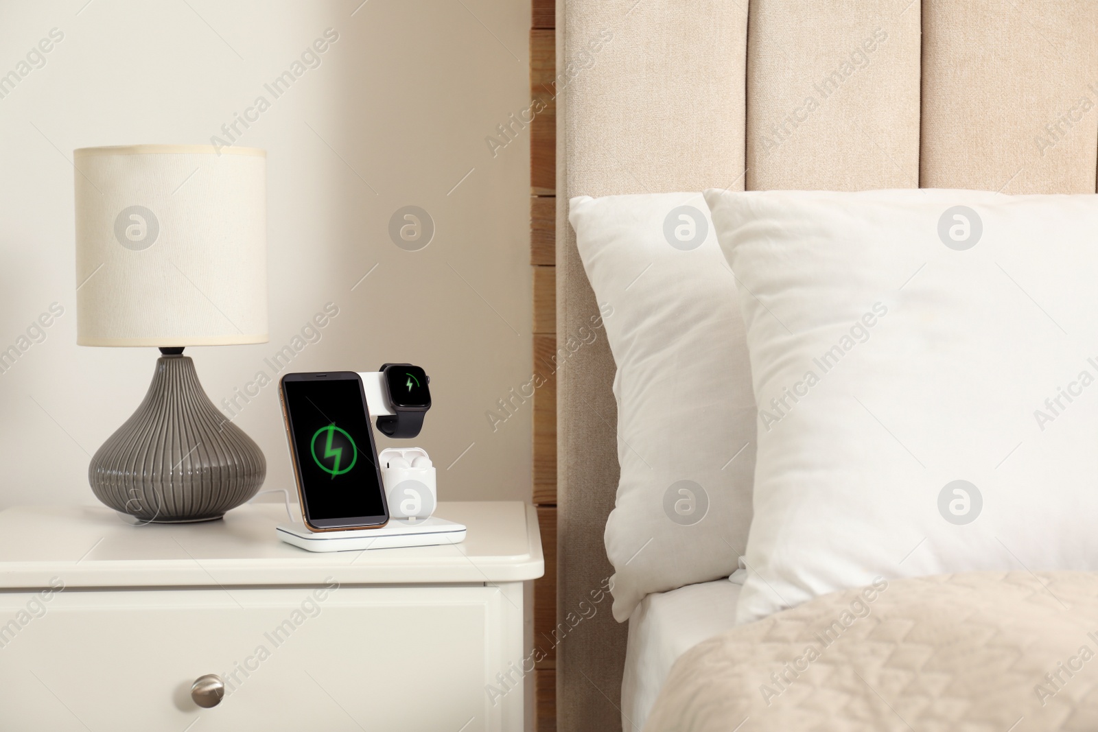 Photo of Different gadgets charging on wireless pad in bedroom