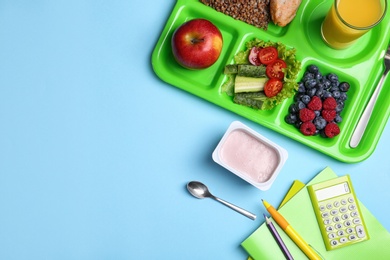 Serving tray of healthy food and stationery on light blue table, flat lay with space for text. School lunch