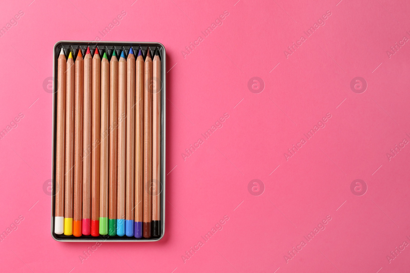 Photo of Box with many colorful pastel pencils on pink background, top view and space for text. Drawing supplies