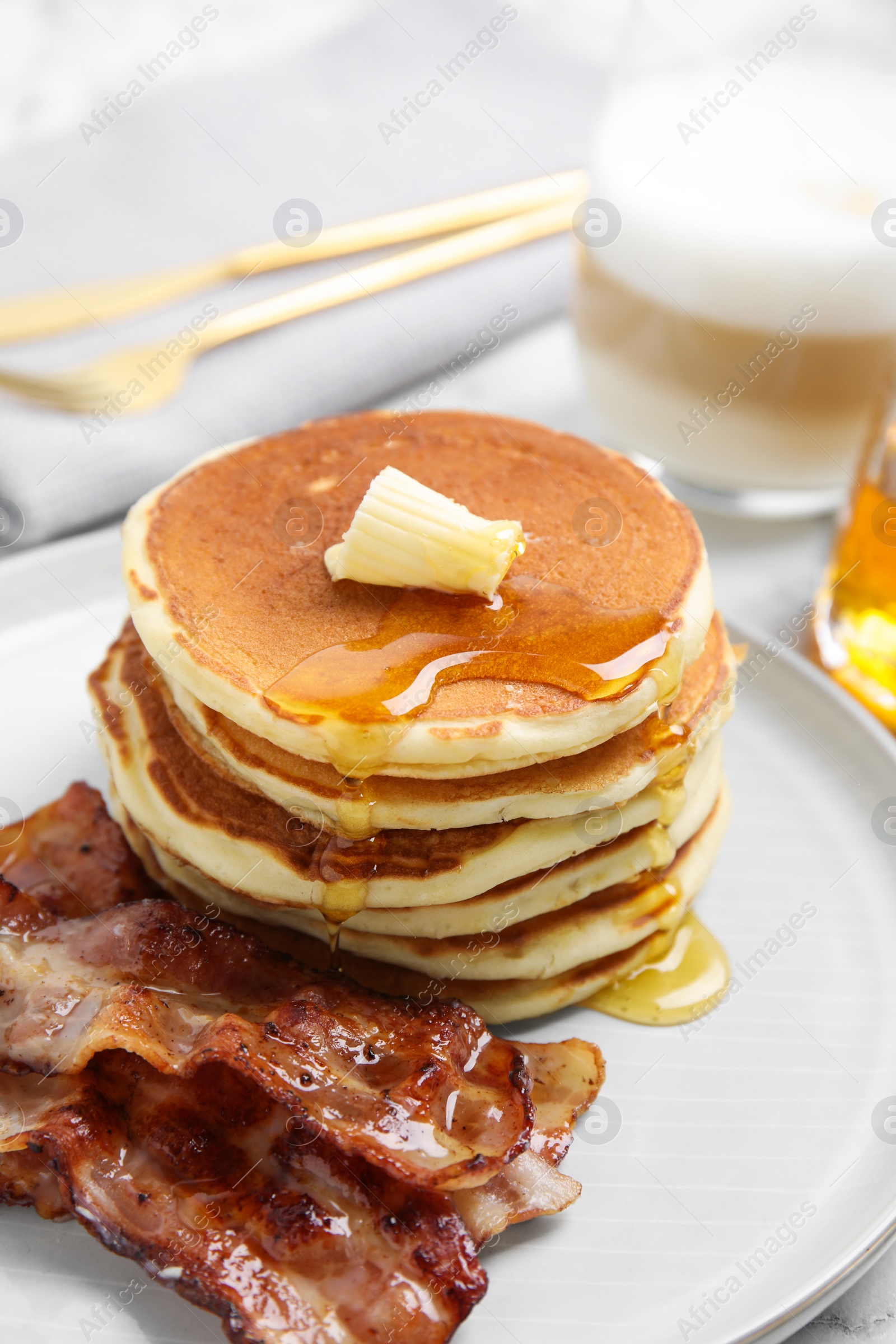 Photo of Delicious pancakes with maple syrup, butter and fried bacon on plate, closeup