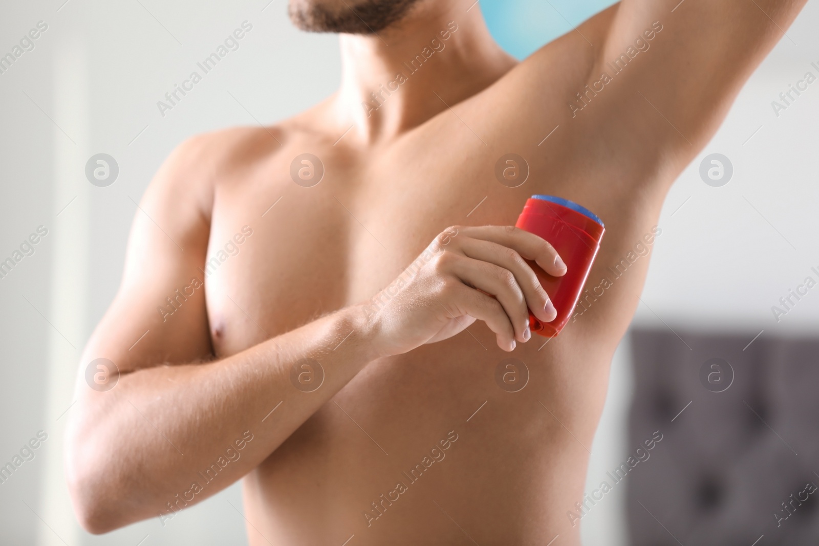 Photo of Handsome young man applying deodorant in room