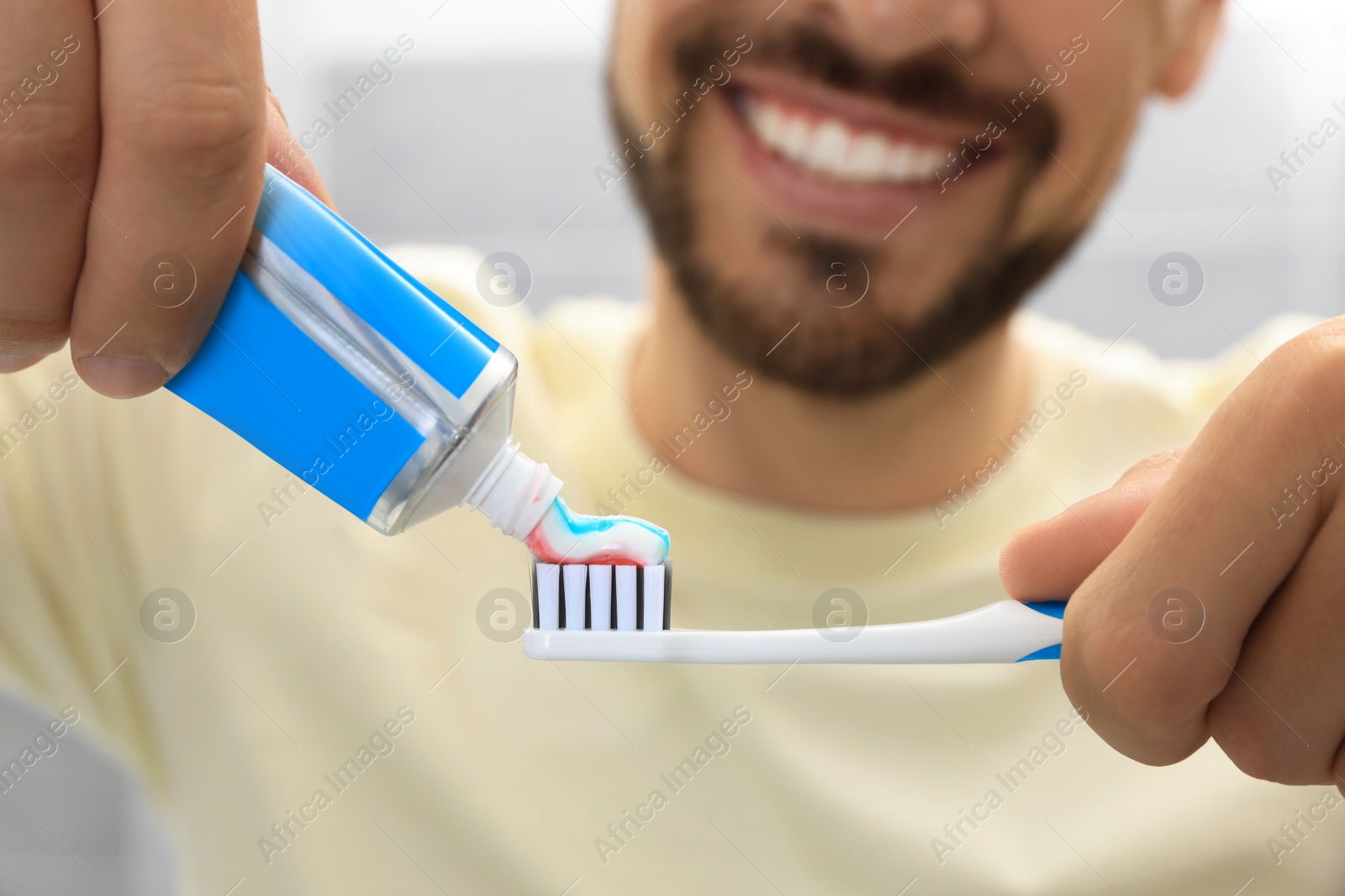 Photo of Man applying toothpaste on brush against blurred background, closeup