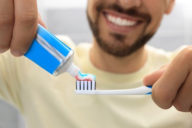 Man applying toothpaste on brush against blurred background, closeup