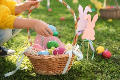 Photo of Little child with basket of Easter eggs in park, closeup