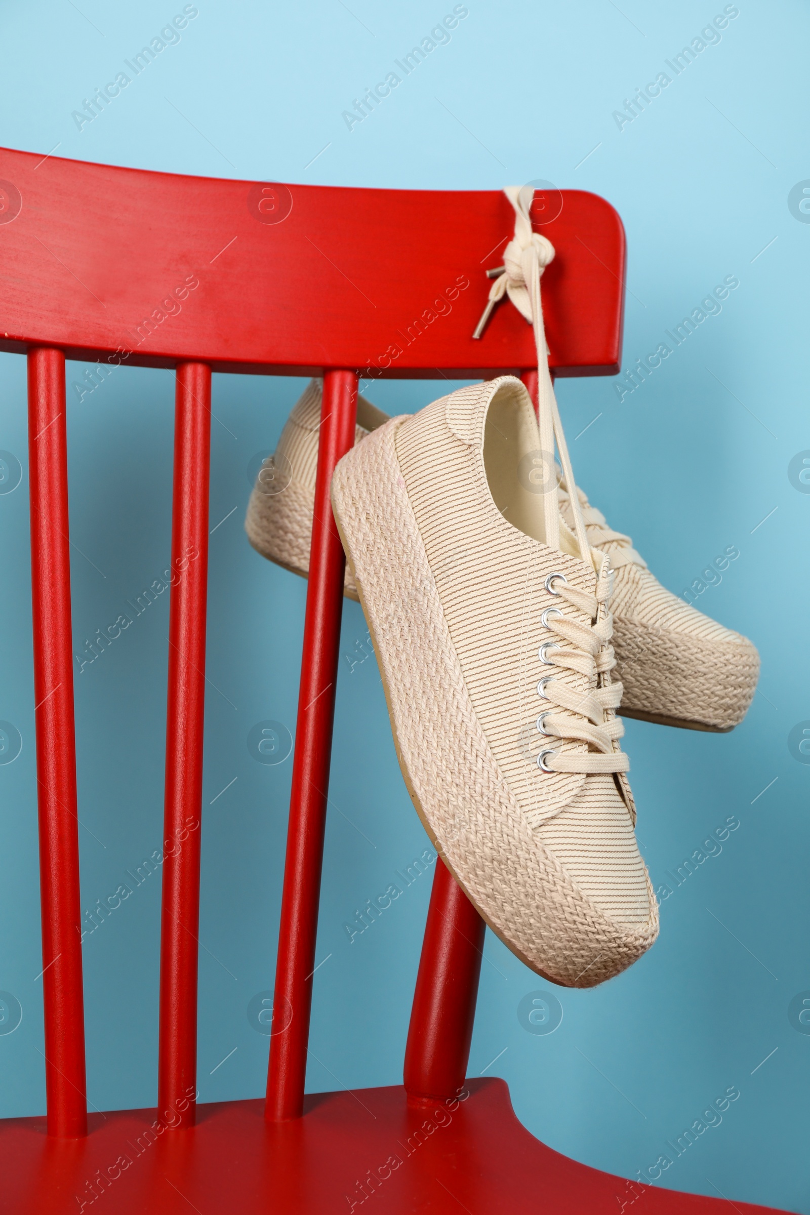 Photo of Pair of stylish sneakers hanging on red chair against light blue background