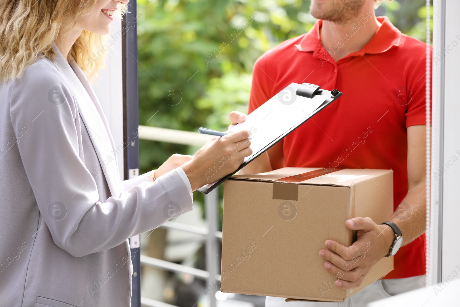 Photo of Young woman signing documents after receiving parcel from courier on doorstep