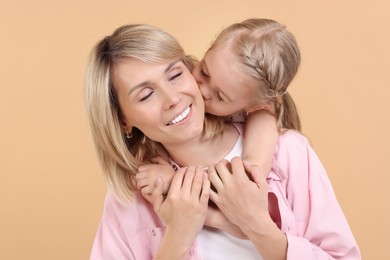 Daughter hugging and kissing her happy mother on beige background