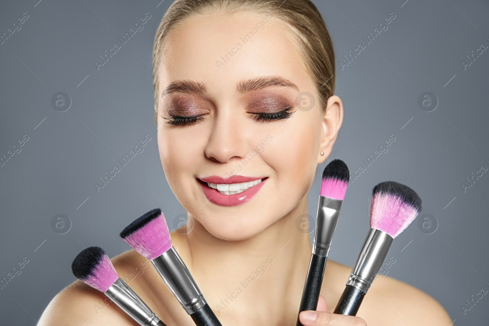 Photo of Beautiful woman with makeup brushes on light grey background