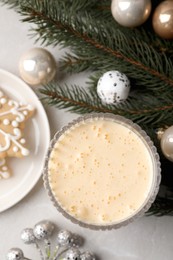 Photo of Glass of delicious eggnog, cookie and decorated fir branch on light table, flat lay