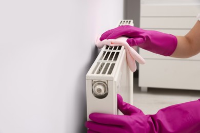 Photo of Woman cleaning radiator with rag indoors, closeup