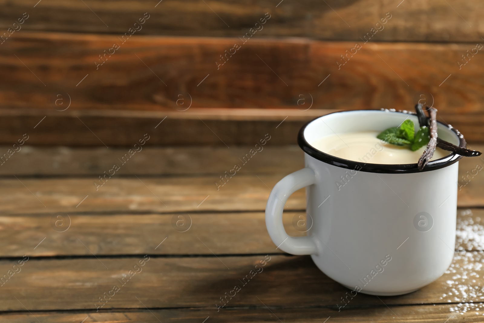 Photo of Mug with vanilla pudding, sticks and fresh mint on wooden table