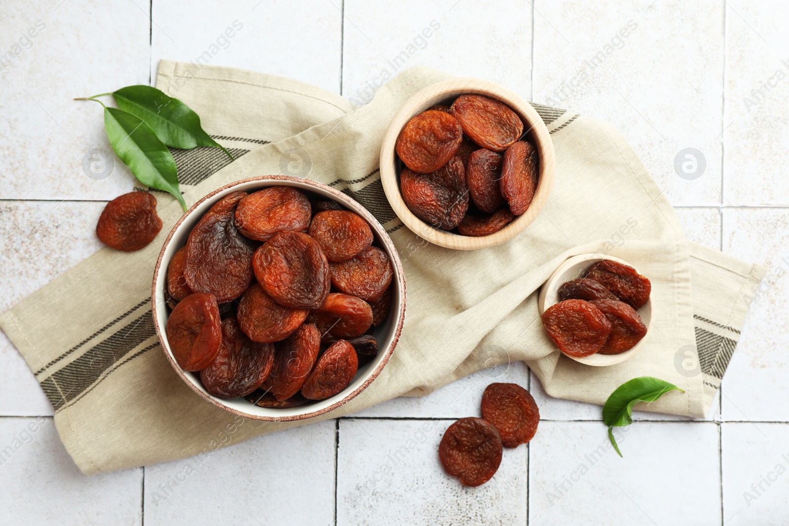 Photo of Tasty apricots with leaves on white tiled table, flat lay. Dried fruits