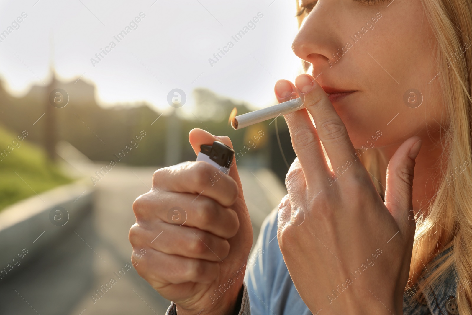 Photo of Young woman lighting cigarette outdoors, closeup of hands