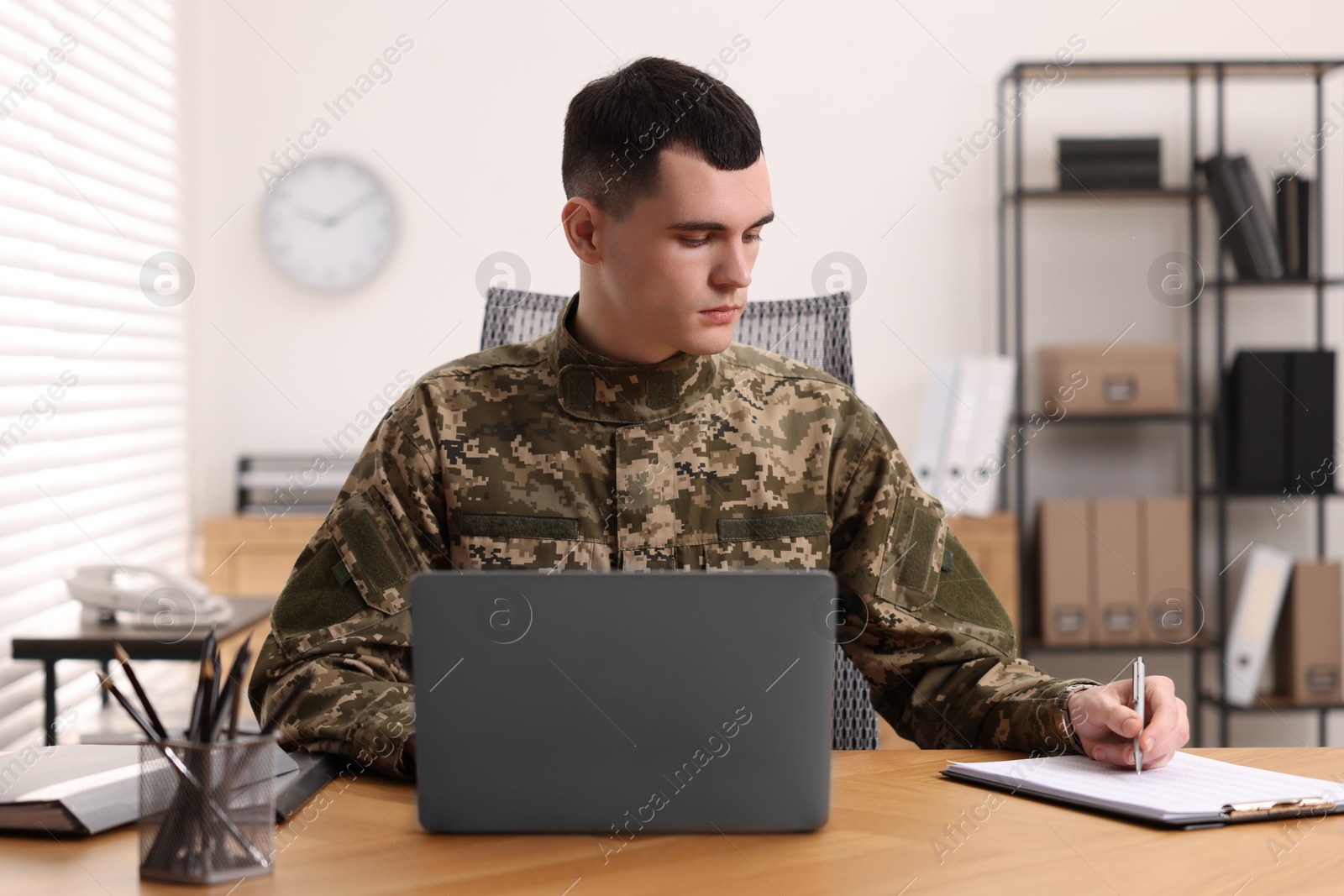 Photo of Military service. Young soldier working at wooden table in office