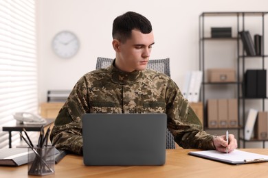 Photo of Military service. Young soldier working at wooden table in office