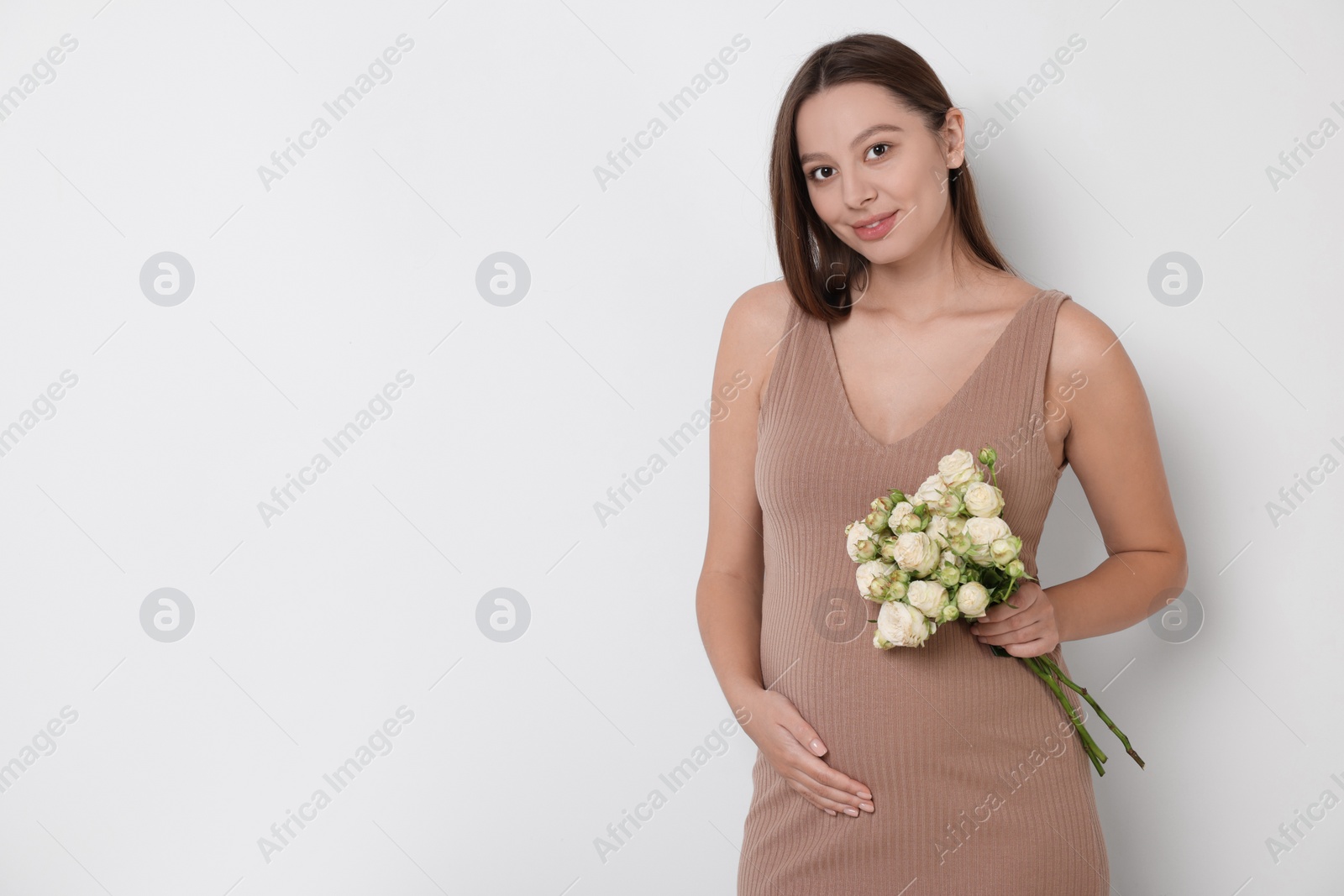 Photo of Beautiful pregnant woman in beige dress with bouquet of roses on white background, space for text