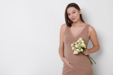 Photo of Beautiful pregnant woman in beige dress with bouquet of roses on white background, space for text