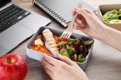 Photo of Woman eating healthy products high in vegetable fats near laptop at wooden table, closeup