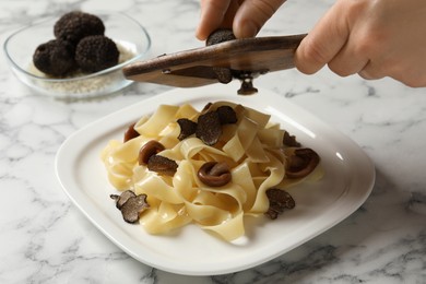 Photo of Woman slicing truffle onto tagliatelle at white marble table, closeup