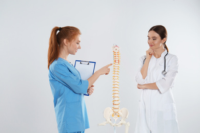 Photo of Professional orthopedist with human spine model teaching medical student against light background