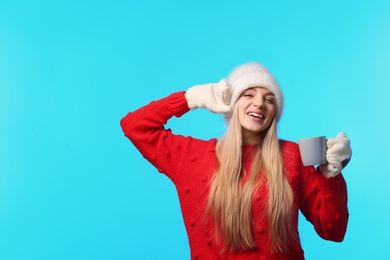 Portrait of emotional young woman in stylish hat, sweater and mittens with cup on color background, space for text. Winter atmosphere