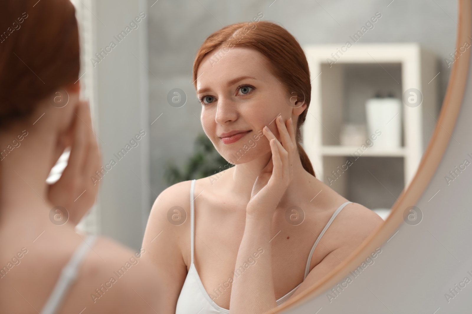 Photo of Beautiful woman with freckles near mirror in bathroom