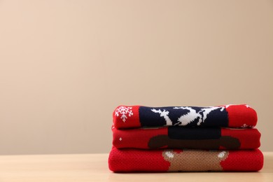 Stack of different Christmas sweaters on table against beige background. Space for text
