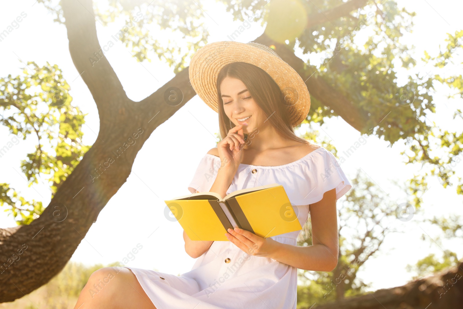 Photo of Young woman reading book near tree in park