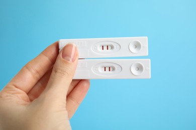 Photo of Woman holding two disposable express tests for hepatitis on light blue background, closeup
