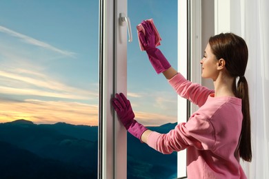 Photo of Young woman cleaning window glass with rag at home, space for text