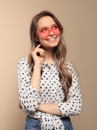 Portrait of beautiful young woman with heart shaped sunglasses on color background