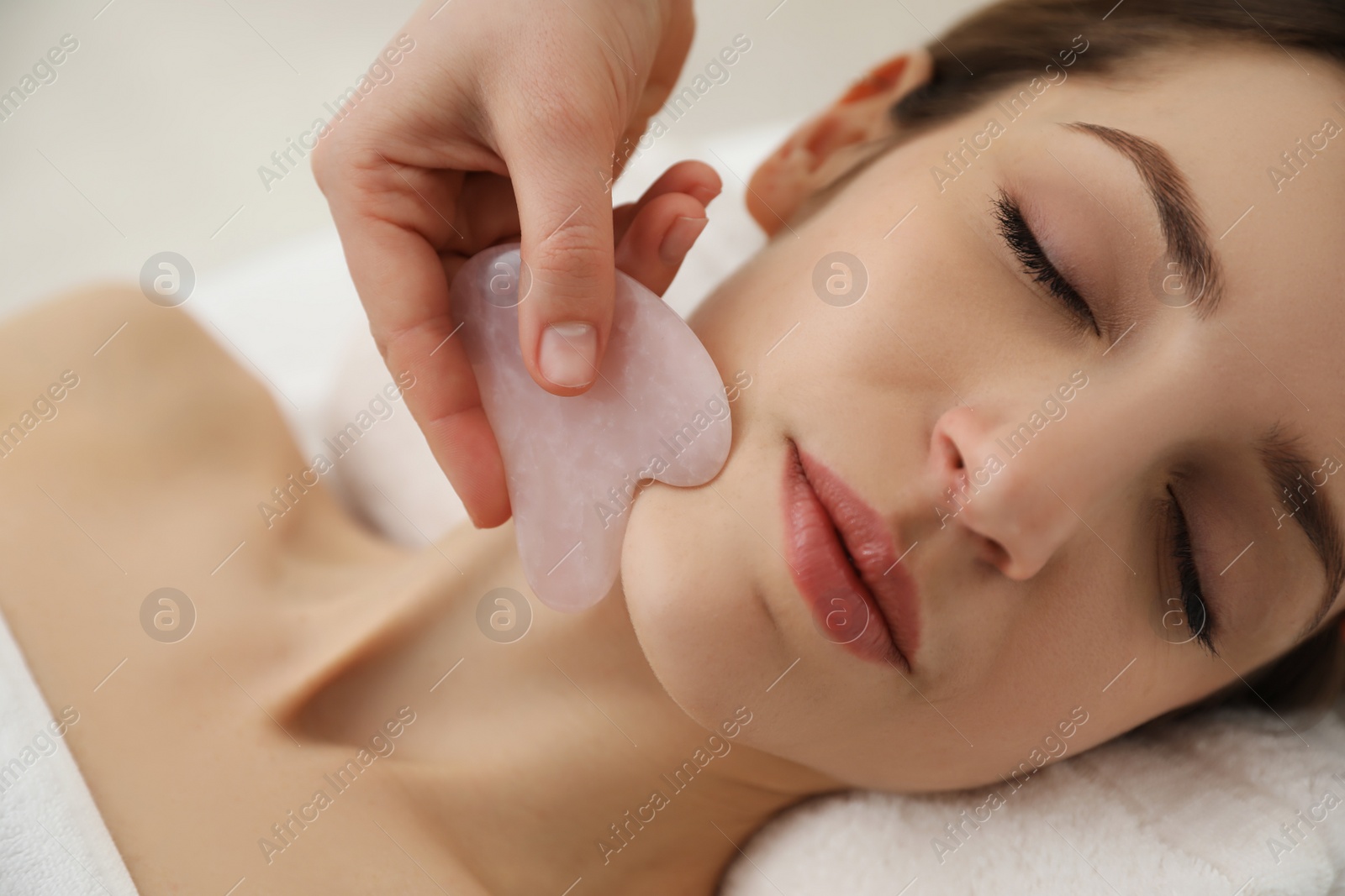 Photo of Young woman receiving facial massage with gua sha tool in beauty salon, closeup