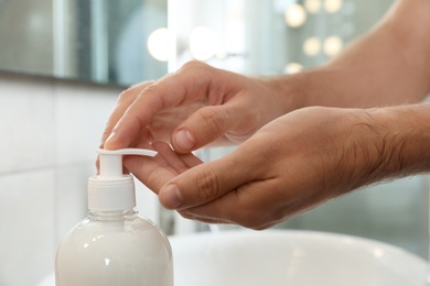 Photo of Man applying liquid soap on hand in bathroom, closeup