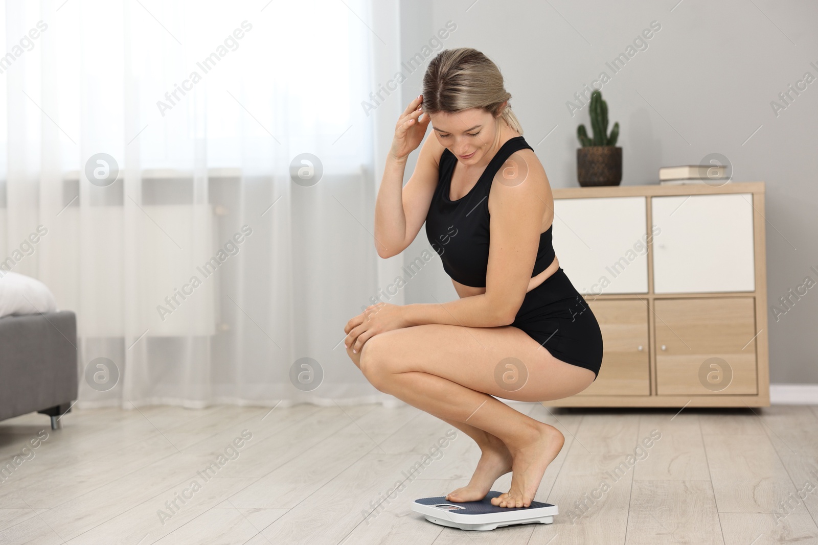Photo of Happy woman standing on floor scales at home