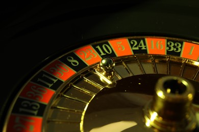 Photo of Roulette wheel with ball on black background, closeup. Casino game