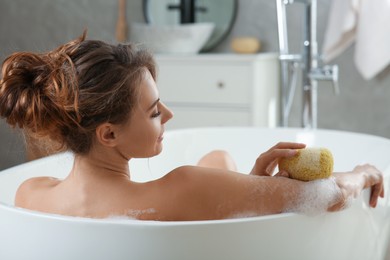 Beautiful woman with sponge taking bath indoors