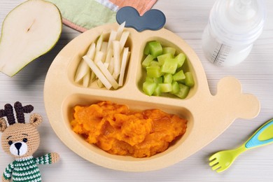 Photo of Healthy baby food. Section plate with delicious pumpkin puree and vegetables on white wooden table, flat lay
