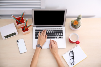 Female blogger using laptop at table, top view. Blank screen for mockup