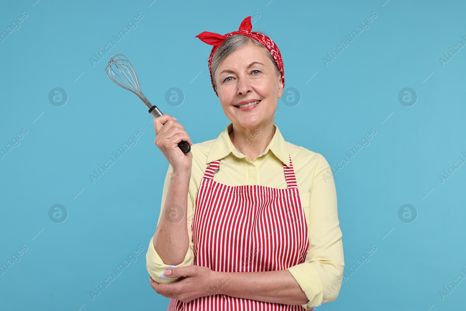 Photo of Happy housewife with whisk on light blue background