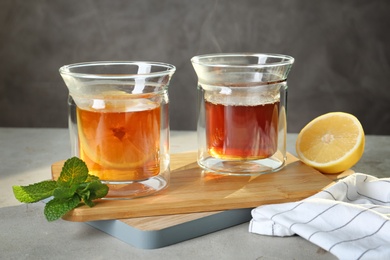 Photo of Wooden board with glasses of hot tea and lemon on table